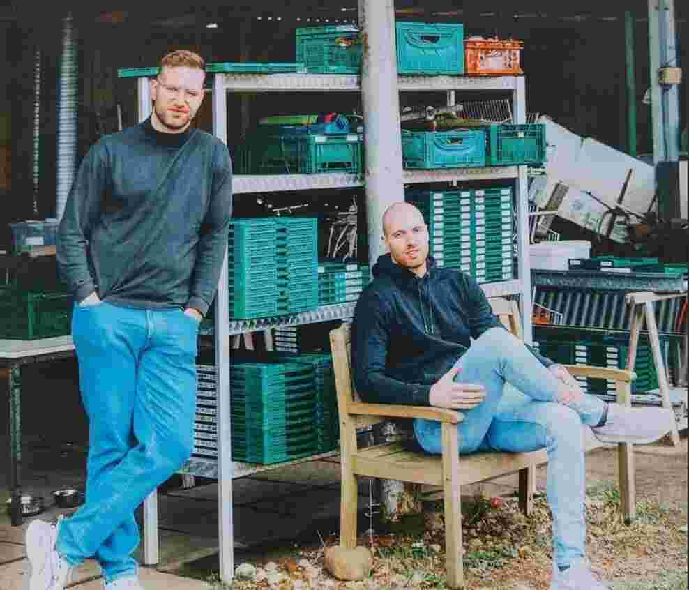 Marco und Maik Möller sind im Mittelpunkt. Marco sitzt und Maik steht neben ihm. Im Hintergrund sieht man Gemüsekisten.