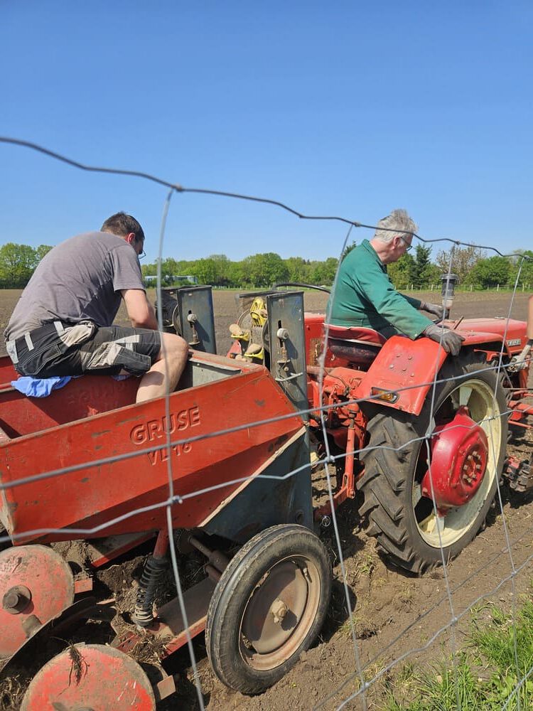 Zwei Männer arbeiten auf einem Feld mit einem roten Traktor und einem Anhänger, der mit 