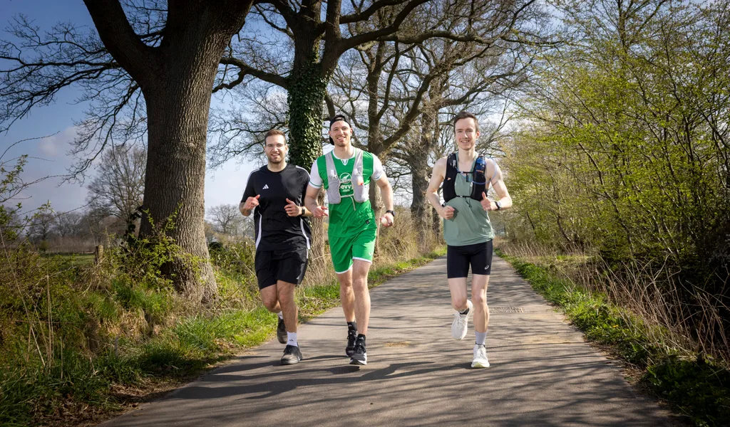 Das Bild zeigt drei Personen, die auf einem Weg durch eine natürliche Umgebung joggen. Sie tragen Sportkleidung und scheinen sich auf ein Lauftraining oder einen Wettkampf vorzubereiten. Die Umgebung ist ländlich, mit Bäumen und Grünflächen entlang des Weges. Die Läufer wirken konzentriert und entschlossen, was auf eine ernsthafte sportliche Aktivität hindeutet.  Dieses Bild könnte im Zusammenhang mit dem Artikel über die Möller-Brüder stehen, die sich auf ihren ersten Marathon vorbereiten, wie in der 