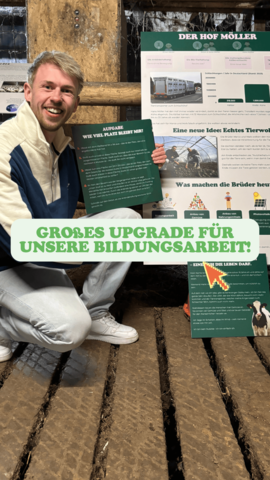 Das Bild zeigt eine Person, die kniet und ein Schild mit der Aufschrift "Großes Upgrade für unsere Bildungsarbeit!" hält. Die Person trägt eine weiße Hose, ein weißes Hemd und eine blaue Jacke und lächelt in die Kamera. Im Hintergrund sind mehrere Poster und Informationsblätter zu sehen, die auf einem Holzboden ausgelegt sind. Die Poster scheinen Informationen über den Hof Möller und deren Bildungsarbeit zu enthalten. Der Text auf den Postern ist nicht vollständig lesbar, aber es scheint um Themen wie Landwirtschaft, Bildung und nachhaltige Praktiken zu gehen. Das Logo "Der Hof Möller" ist auf einem der Poster sichtbar, was darauf hinweist, dass die Person möglicherweise mit diesem Betrieb verbunden ist.