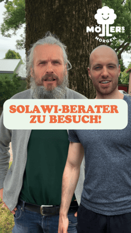 Das Bild zeigt zwei Personen, die nebeneinander stehen und in die Kamera lächeln. Die Person auf der linken Seite hat einen langen, grauen Bart und trägt ein graues Sweatshirt über einem grünen T-Shirt sowie eine Jeans. Die Person auf der rechten Seite ist glattrasiert und trägt ein graues T-Shirt und eine dunkle Hose. Beide Personen stehen vor einem Baum und einer grünen Landschaft, was auf eine ländliche Umgebung hindeutet. Über dem Bild ist ein Text mit der Aufschrift "Solawi-Berater zu Besuch!" zu sehen, was darauf hindeutet, dass es sich bei den Personen möglicherweise um Berater für Solidarische Landwirtschaft (Solawi) handelt, die den Betrieb besuchen. Das Logo "Möllers Morgen" ist in der oberen rechten Ecke des Bildes sichtbar, was darauf hinweist, dass die Personen mit diesem Betrieb verbunden sind.