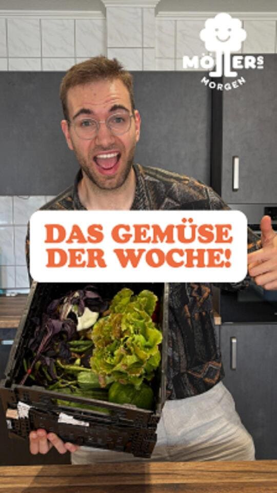 Ein lächelnder Mann mit Brille hält eine Kiste mit frischem Gemüse, darunter verschiedene Salatsorten wie Lollo Rosso, Eichblatt und Kopfsalat. Im Hintergrund ist eine moderne Küche zu sehen. Über dem Bild steht in großen, orangefarbenen Buchstaben: DAS GEMÜSE DER WOCHE! Das Logo von Möllers Morgen ist in der oberen rechten Ecke sichtbar.