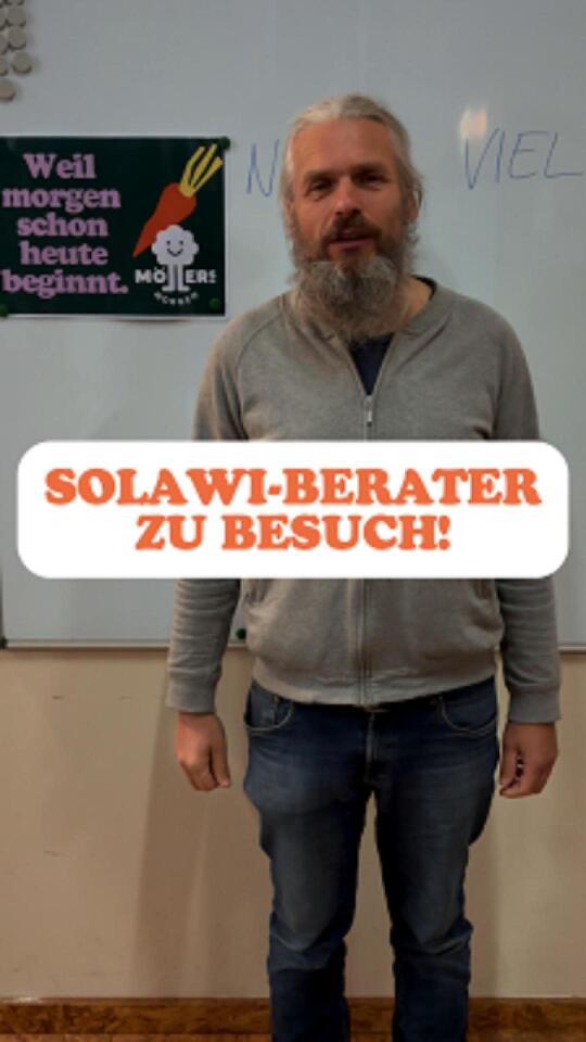 Ein Mann mit langem Bart und langen Haaren steht vor einer Whiteboard-Tafel. Er trägt eine graue Jacke und Jeans. Im Hintergrund ist ein Plakat mit der Aufschrift "Weil morgen schon heute beginnt. Möllers Gemüse" und einer Karotten-Illustration zu sehen. Im Vordergrund des Bildes steht in großen, orangefarbenen Buchstaben: SOLAWI-BERATER ZU BESUCH! Die Stimmung wirkt informativ und freundlich.