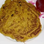 Ein goldbraun gebratener Kartoffel-Möhren-Puffer auf einem weißen Teller, knusprig und appetitlich zubereitet, begleitet von einem Klecks Rote-Bete-Dip.