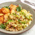 Ein herzhafter Teller mit **Bratkartoffeln und Rahmwirsing**. Die Kartoffeln sind goldbraun und knusprig gebraten, während der Rahmwirsing in einer cremigen Sauce mit frischen Petersilienblättern garniert ist. Das Gericht wirkt deftig, lecker und perfekt für eine gemütliche Mahlzeit! Ein Genuss für alle, die traditionelle Küche lieben.