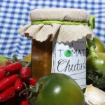Das Bild zeigt ein Glas mit **veganem Chutney aus grünen Tomaten**, das mit einem Stoffdeckel verschlossen ist. Das Etikett auf dem Glas ist handschriftlich beschriftet und trägt die Aufschrift **