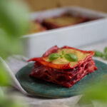 Stück vegane Rote-Bete-Lasagne auf einem grünen Teller, geschichtet mit intensiver Rote-Bete-Füllung und überbacken mit goldener 