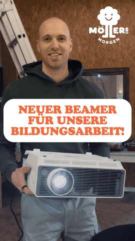 Lächelnder Mann hält einen neuen Beamer in den Händen, im Hintergrund ist das Logo von Möllers Morgen zu sehen, Textüberlagerung lautet Neuer Beamer für unsere Bildungsarbeit!