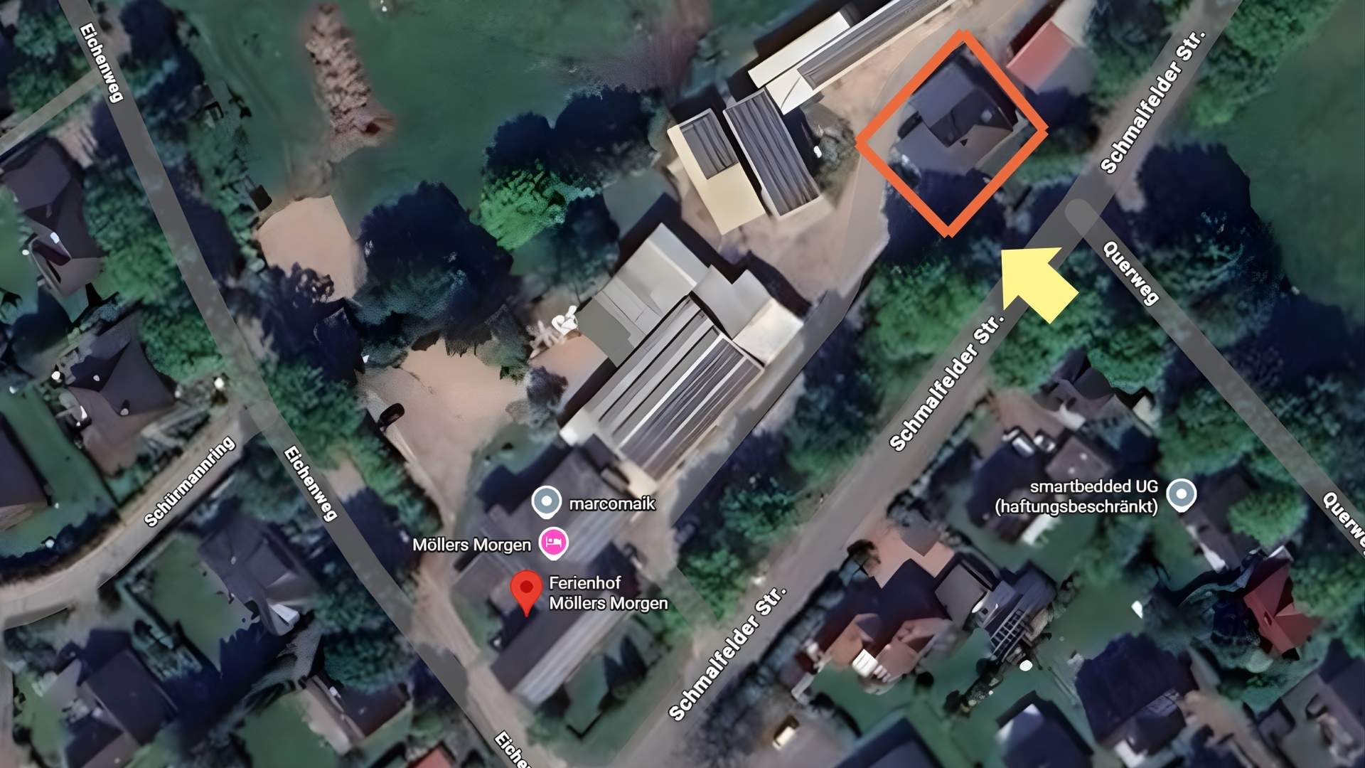 Luftaufnahme des Ferienhofs "Möllers Morgen" in Schleswig-Holstein. Der Hof ist durch ein orangefarbenes Rechteck markiert und liegt an der Ecke Schmalfelder Straße und Querweg. Ein gelber Pfeil zeigt auf ein Gebäude oder eine spezifische Stelle auf dem Gelände.