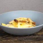 Schale mit veganem Kartoffel-Kohlrabi-Auflauf, goldbraun überbacken und knusprig, serviert auf einem dunklen Holztisch.