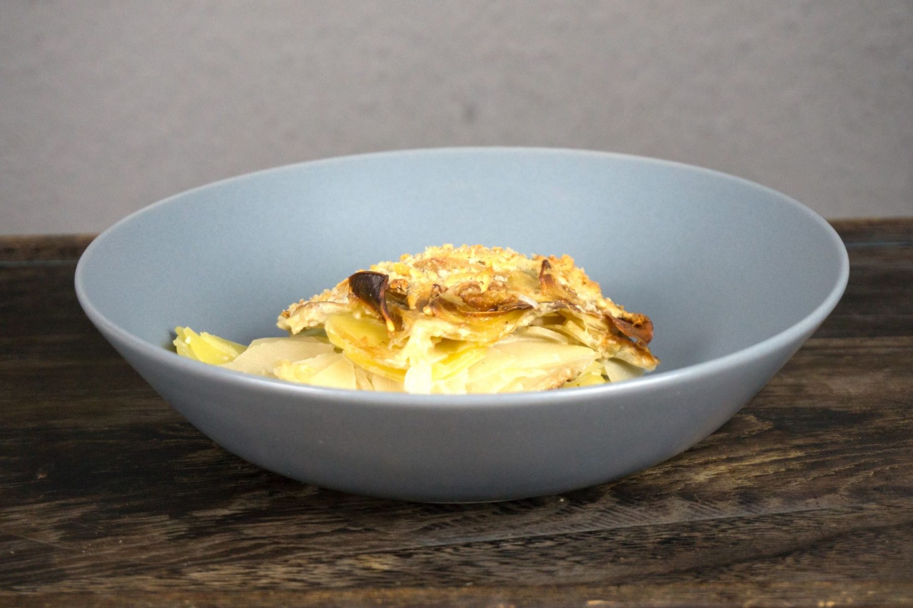 Schale mit veganem Kartoffel-Kohlrabi-Auflauf, goldbraun überbacken und knusprig, serviert auf einem dunklen Holztisch.