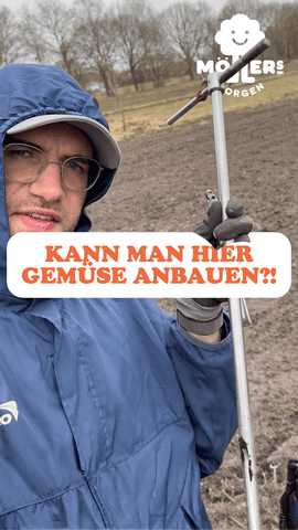 Ein vertikales Beitragsbild zeigt einen Mann in einer blauen Regenjacke mit Kapuze und einer hellen Kappe, der direkt in die Kamera blickt. Er steht auf einem freien Feld und hält einen metallischen Bodenprobenentnehmer (Pürckhauer) in der Hand. Im Vordergrund liegt ein weißes Textfeld mit der orangefarbenen Aufschrift: „KANN MAN HIER GEMÜSE ANBAUEN?!“. Oben rechts ist das weiße Logo von „Möllers Morgen“ mit dem lächelnden Wolken-Symbol platziert. Der Hintergrund zeigt eine herbstliche oder winterliche Ackerlandschaft mit kahlen Bäumen im Fernbereich.